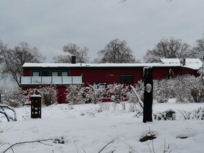 A red building with a balcony, surrounded by snow-covered vegetation. - Findling - Kunsthof Salsitz (Lohme auf Rügen)