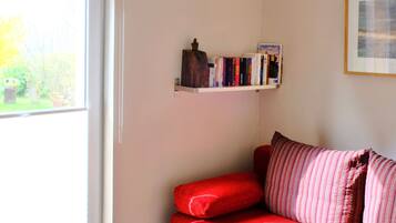 A room with a red sofa, a bookshelf, a framed picture on the wall, and a door leading to a garden.