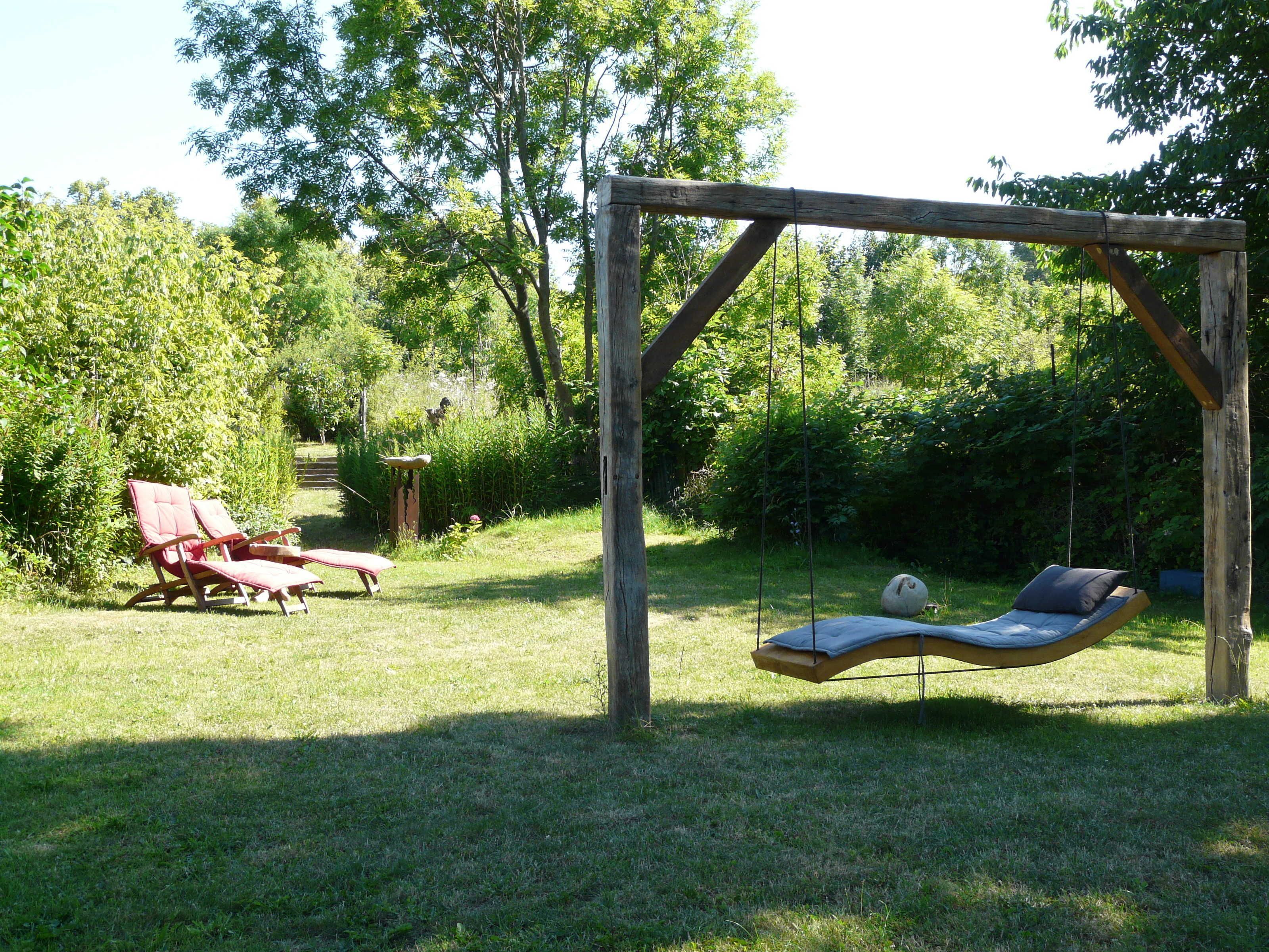 Ein Garten mit einer Schaukel und einem roten Liegestuhl.