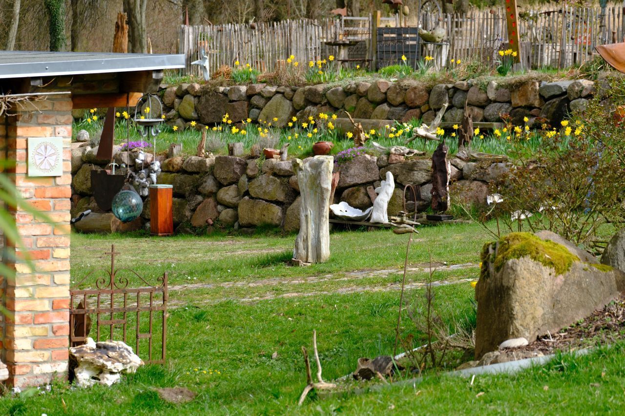 Un jardin rustique agrémenté d’un mur de pierres, d’une clôture en bois et d’une variété de plantes et de fleurs.