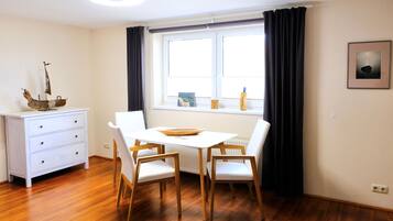 A dining area with a white table, wooden chairs, a white cabinet, and a window with black curtains.