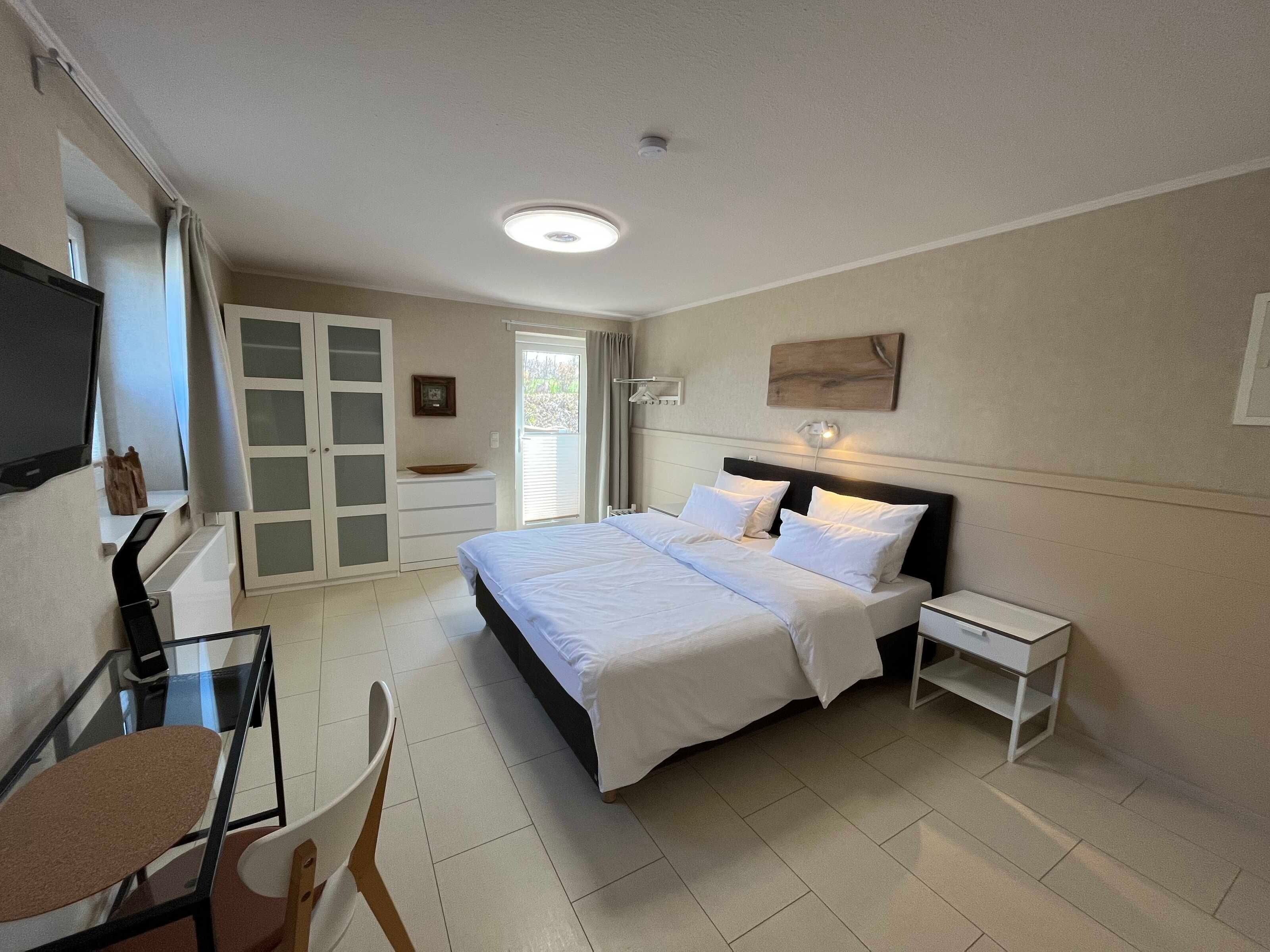 Une chambre d’hôtel comprenant un lit, des tables de chevet, une télévision, un bureau avec une chaise et une porte-fenêtre coulissante donnant sur un balcon.