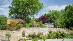 A stone staircase leading to a house surrounded by lush greenery and flowering plants.