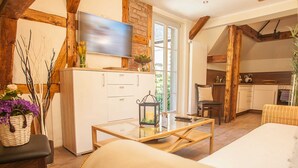 A cozy room with a bed, a TV, a small table with a candle, and a kitchen area visible through an open door.