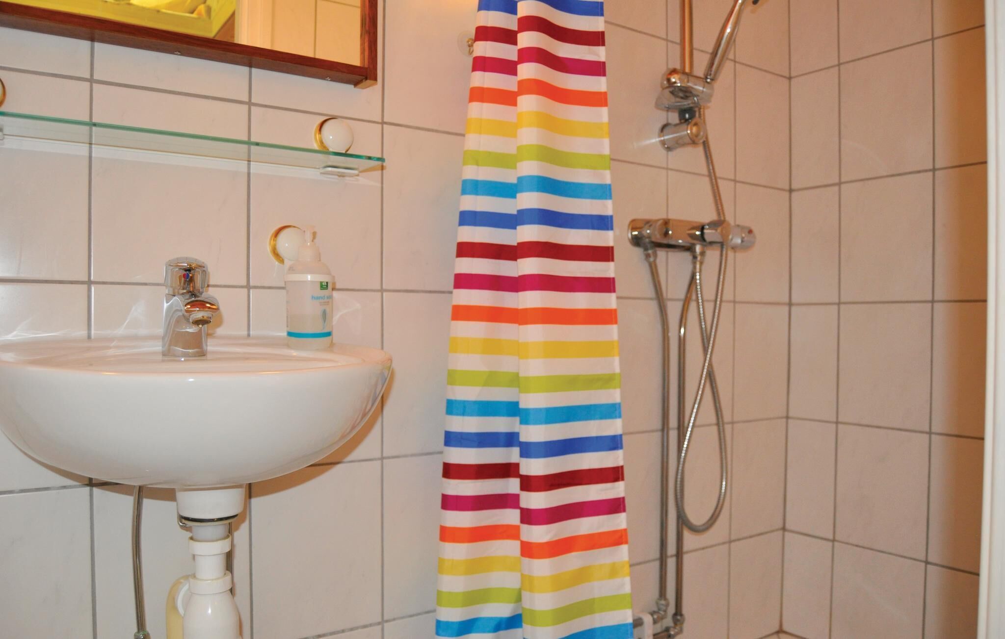 Een badkamer met een wit wastafelmeubel, een glazen plank, een gestreept douchegordijn en een handzeepdispenser.