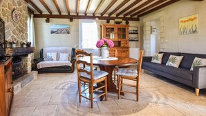 Un salon chaleureux avec une cheminée en pierre, des meubles en bois et un coin repas comprenant une table ronde et des chaises.