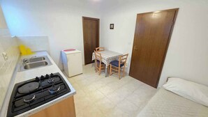 A compact kitchen with a gas stove, a sink, and a small refrigerator. There is a dining table with two chairs and a single bed with a pillow. - Holiday apartment with terrace (Crikvenica)