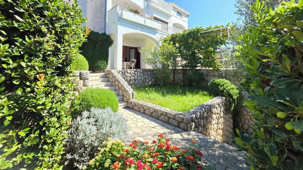 A two-story building with a balcony, surrounded by lush greenery and a stone pathway leading to the entrance. - Holiday apartment with terrace (Crikvenica)