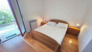 A bedroom with a wooden bed, a nightstand, a lamp, and a view of the outdoors. - Holiday apartment with terrace (Crikvenica)