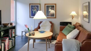 Un salon avec une table ronde, un canapé, une bibliothèque et deux lampes fixées au mur.