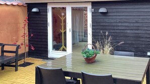Une terrasse avec une table et des chaises, une porte-fenêtre coulissante et un petit jardin avec des plantes.