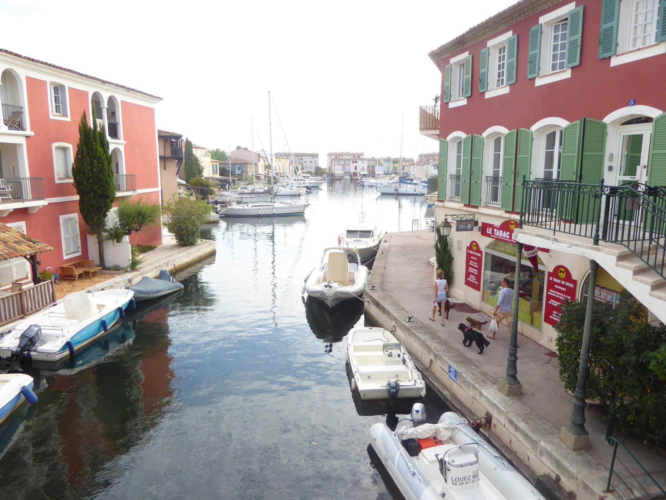 A narrow canal with boats docked on both sides, flanked by buildings with balconies and a café.
