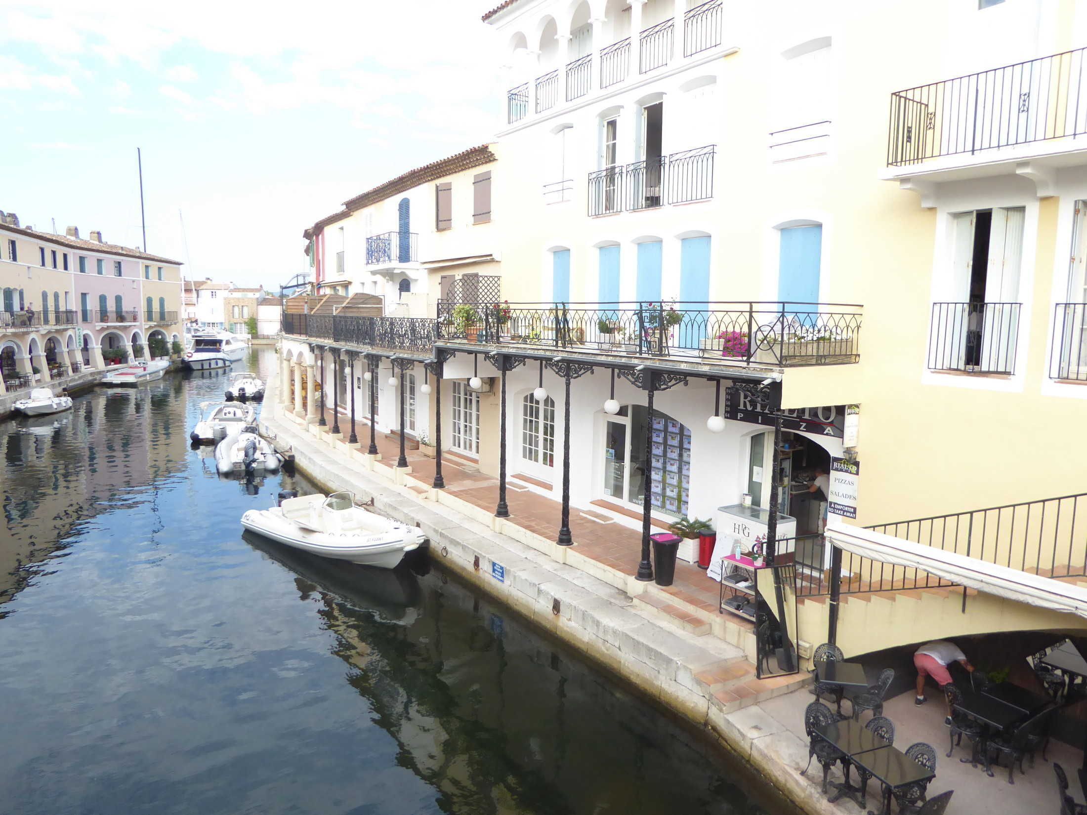 Un canal con barcos, un restaurante con terraza y edificios con balcones.