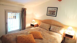 A bedroom with a bed, two pillows, a nightstand, a lamp, a window with curtains, and a framed picture on the wall. - House - House btw. Cogolin and St. Tropez (Cogolin)