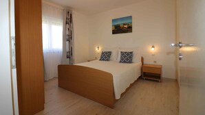 Une chambre à coucher avec un lit en bois, une table de chevet, une lampe fixée au mur et une fenêtre avec des rideaux.