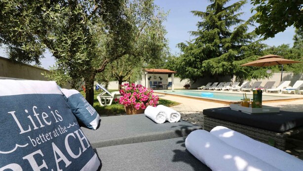 Un espace aménagé au bord de la piscine, avec des chaises longues, une serviette et un panneau sur lequel on peut lire : « La vie est plus belle à la plage. »