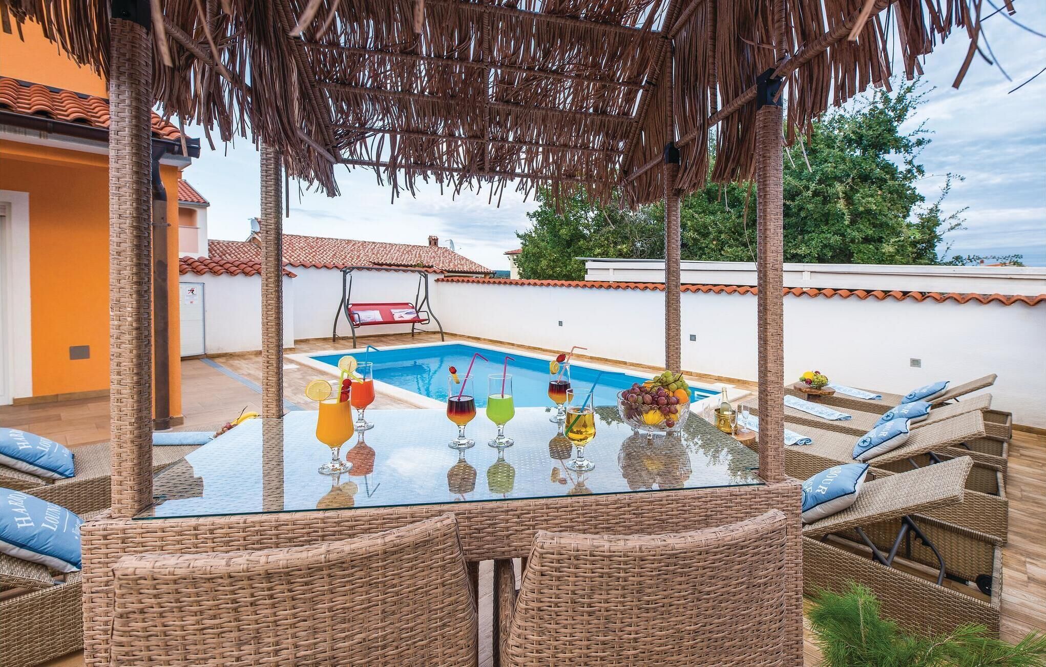 A poolside area with wicker furniture and a glass table with drinks.