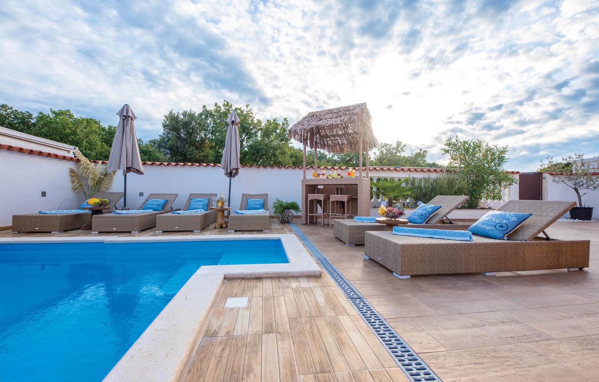 Un área junto a la piscina con sillones de descanso, sombrillas y un bar.