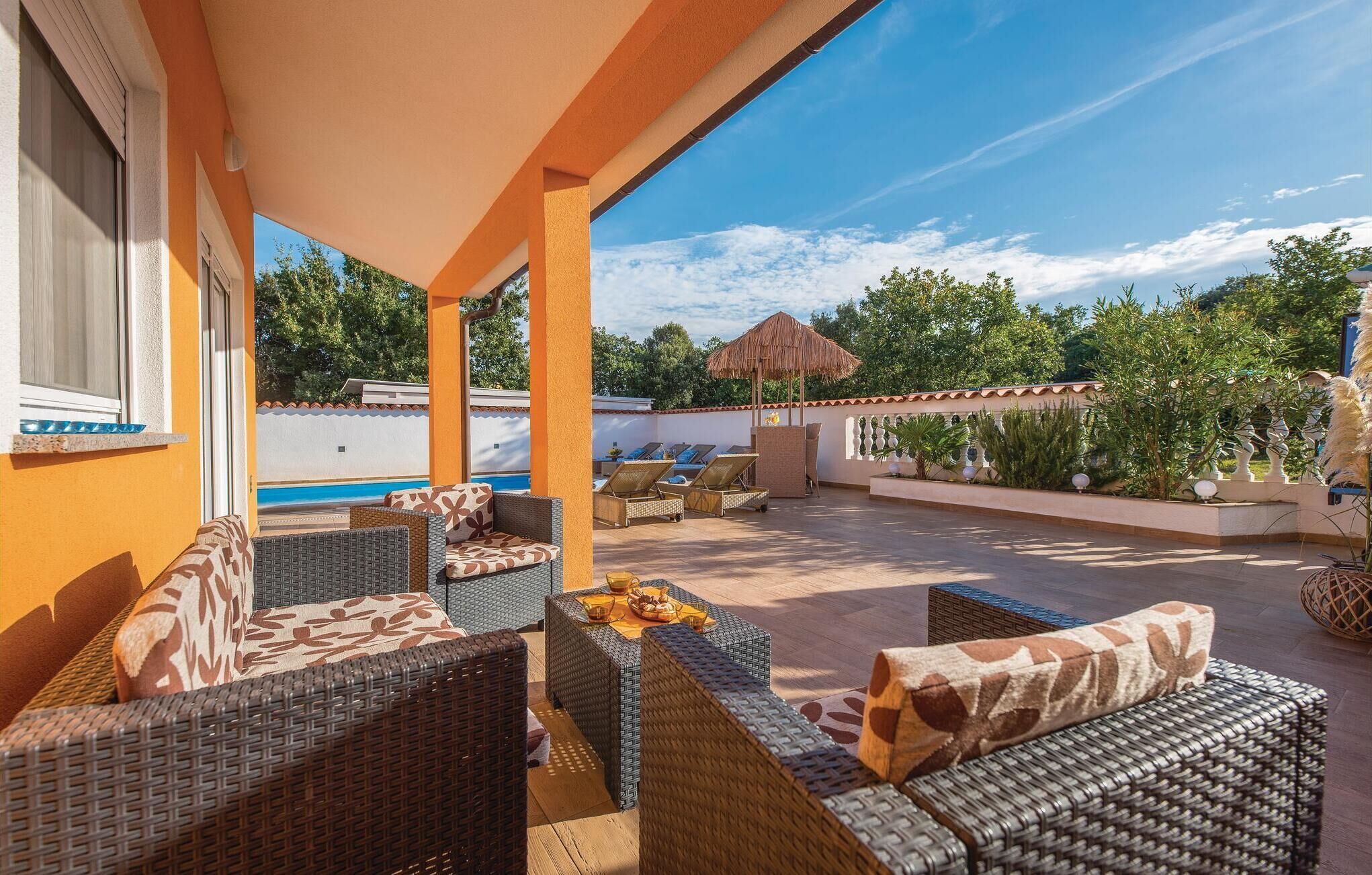 A covered outdoor seating area with wicker furniture, a pool, and a view of the surrounding greenery.