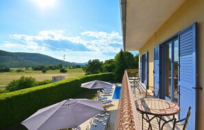 A balcony with outdoor seating, a pool, and a view of the countryside.