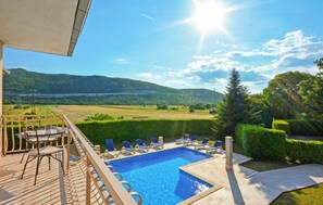 A pool with lounge chairs, a table, and a view of mountains and a lake.