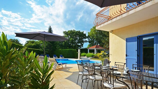 Un espace aménagé au bord de la piscine, comprenant des chaises longues, une table avec des chaises et une pergola dotée d’un parasol.