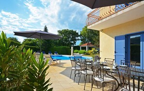 A poolside area with lounge chairs, a table with chairs, and a pergola with an umbrella.