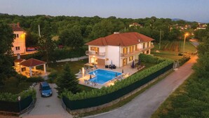 Une maison à deux étages avec une piscine, entourée de verdure et dotée d’une allée pavée.
