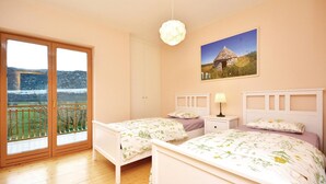 Une chambre avec deux lits, une table de chevet, une lampe, un tableau au mur et un balcon avec vue sur la campagne.