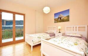 Two single beds with white headboards and floral-patterned bedspreads, a large window with a mountain view, and a painting above.