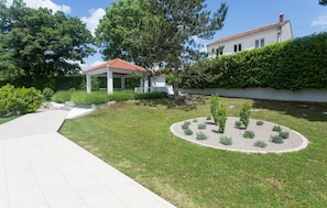 Stroll through the beautifully manicured garden, featuring a tranquil lawn, shrubs, and shaded trees.