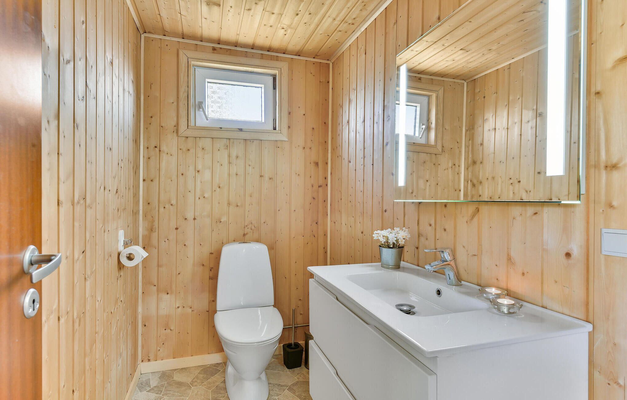 Ein Badezimmer mit Holzvertäfelung, Toilette, Waschbecken und Spiegel.