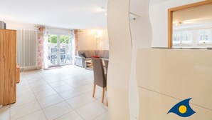 A modern living room with a dining area, a sofa, and a table with chairs. There is a window with curtains and a view of the outdoors. - Apartment (Appartment) Curr 02 Garden Street -. Apartment (Appartment) Curr 02 Garden Street. (Heringsdorf)