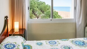 A hotel room with a bed, a bedside table with a lamp, a window with a view of a beach and trees. - Awesome apartment in Santa Susanna (Santa Susanna)