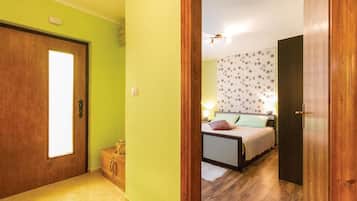 Un passadís condueix a un dormitori amb un llit, una tauleta de nit i una paret amb un disseny floral.