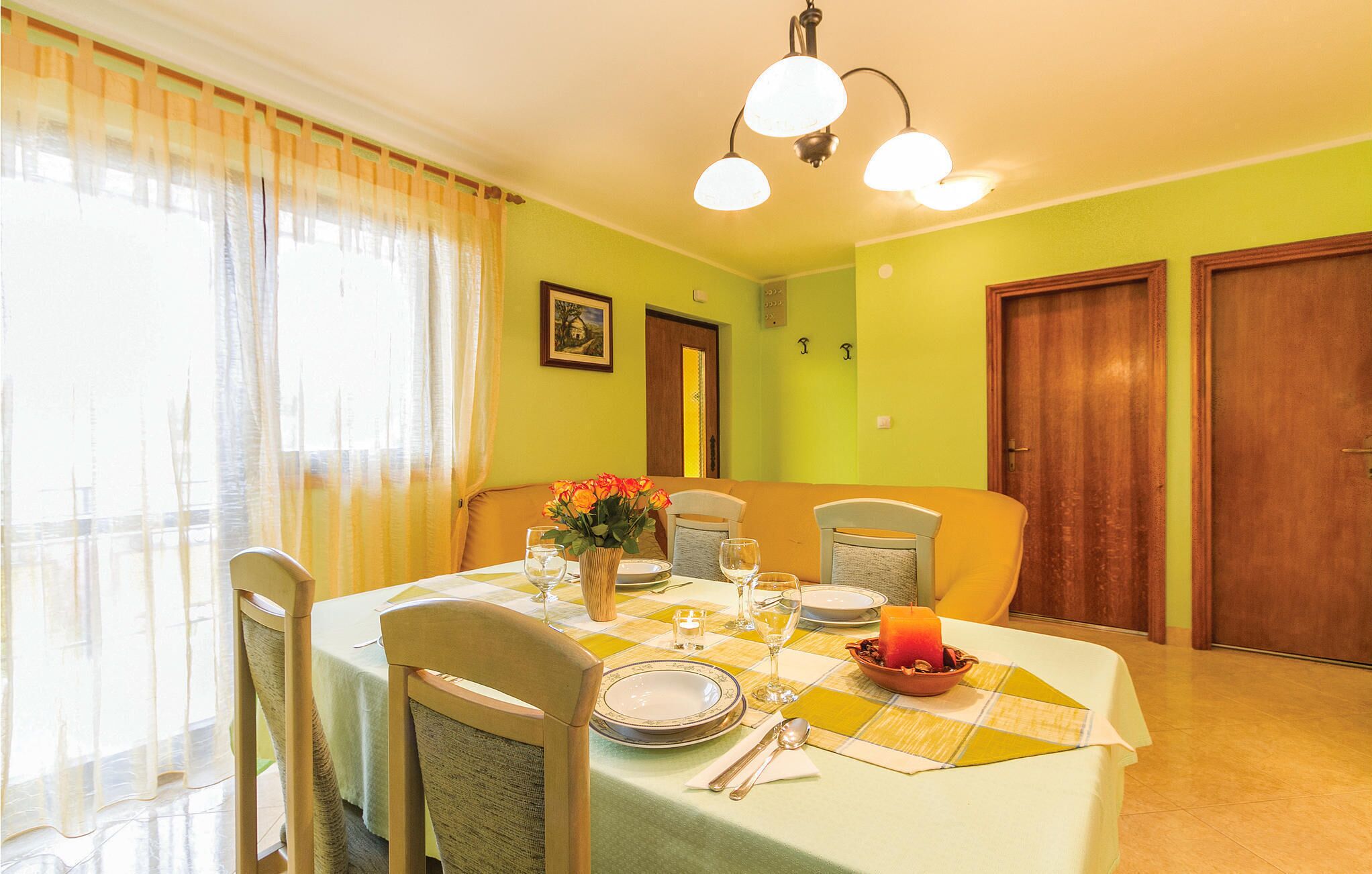 Un comedor con una mesa dispuesta para cuatro personas, sillas, un florero con flores y una vela sobre la mesa.
