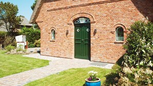 Un edificio de ladrillo con puerta verde, un pequeño porche y un jardín con una planta en maceta.