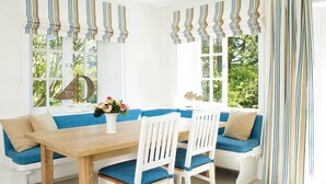 Una habitación luminosa con una mesa de madera y sillas blancas, un banco azul y cortinas a rayas.