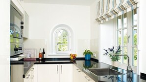 Una cocina moderna con armarios blancos, encimera negra y una ventana con cortinas a rayas.