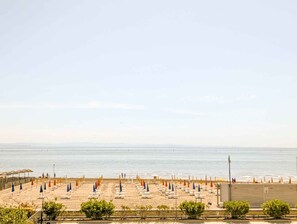 Een strand met rijen parasols en ligbedden, een heldere lucht en de oceaan op de achtergrond.