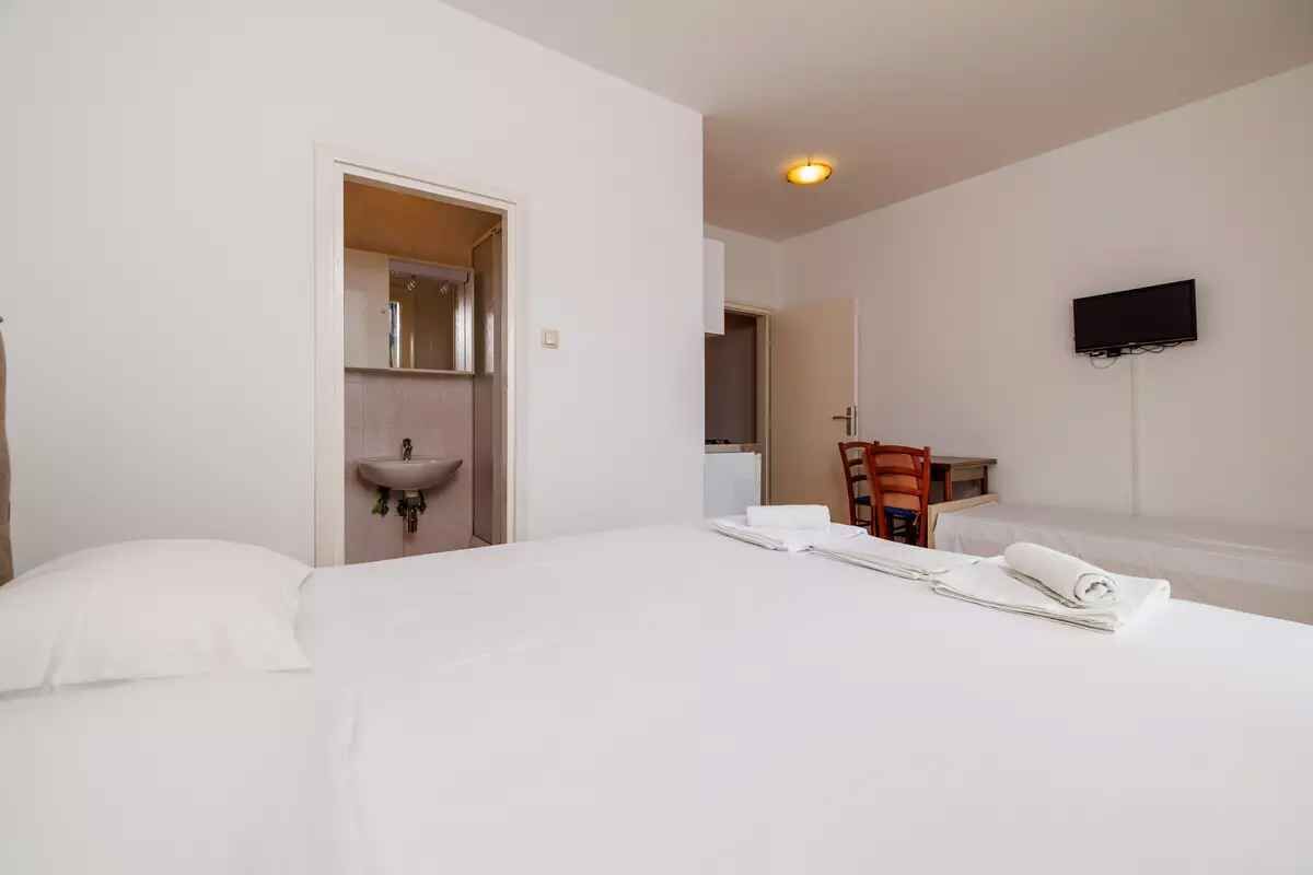 Una camera d'albergo con un letto, un lavandino, una sedia e una TV fissata al muro.