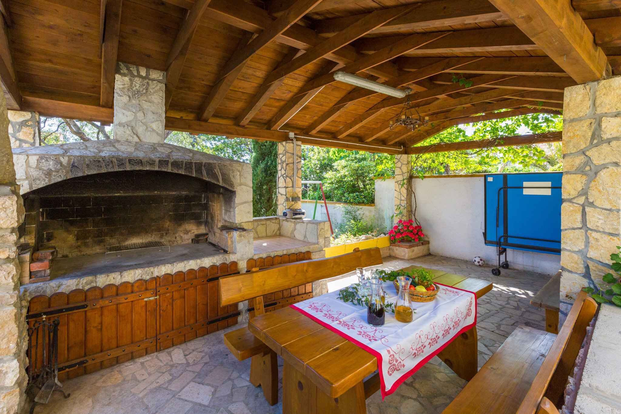Une terrasse extérieure dotée d’une cheminée en pierre, de bancs en bois et d’une table recouverte d’une nappe.