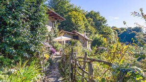 Una casa de piedra rústica con porche de madera, rodeada de abundante vegetación y un sendero de piedra que la conduce.
