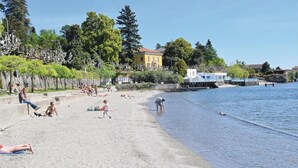 Una playa con gente tomando el sol y nadando, cielo despejado y edificios al fondo.