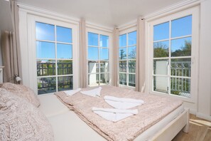 A bedroom with a large bed, multiple windows, and a view of greenery outside.
