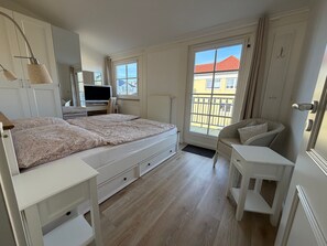 Un dormitorio con cama, escritorio, silla y ventana con vista a edificios.