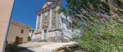 A historic church with a bell tower, stone steps leading up to the entrance, and a garden with lavender.