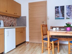 Een kleine keuken met houten kastjes, een witte koelkast, een eettafel met stoelen en een deur.