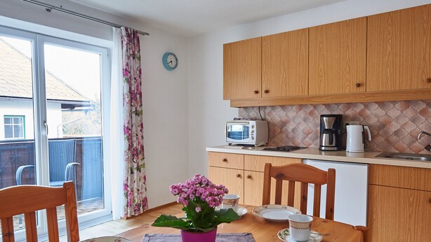 A kitchen with wooden cabinets, a microwave, a coffee maker, and a dining table with chairs.