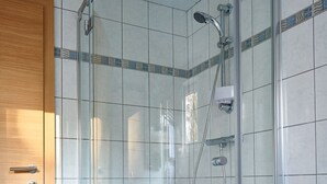 A glass-enclosed shower with a handheld showerhead and a wall-mounted faucet.